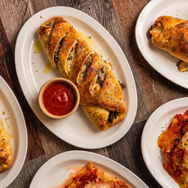 Multiple golden-brown strombolis and cheesy lasagna dishes with marinara sauce on a rustic wooden table.