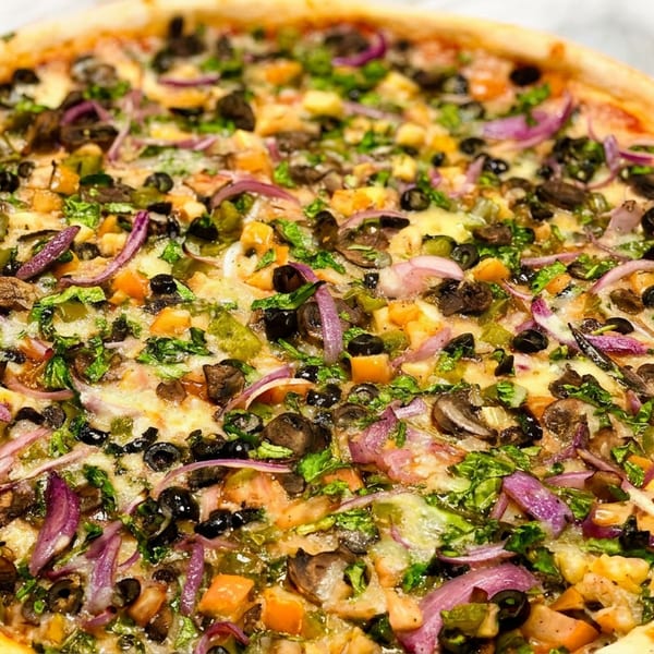 Whole vegetarian pizza topped with olives, red onions, mushrooms, bell peppers, and herbs on a white surface.