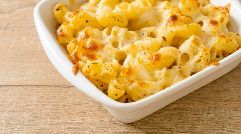 Baked macaroni and cheese in a white dish with melted, browned cheese on a wooden table.