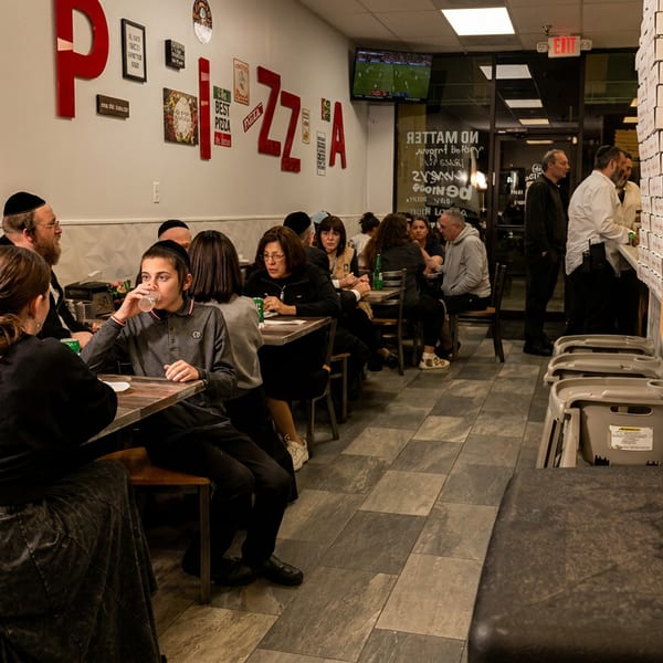 Diners enjoy meals at tables in a casual pizza restaurant with stacked pizza boxes.